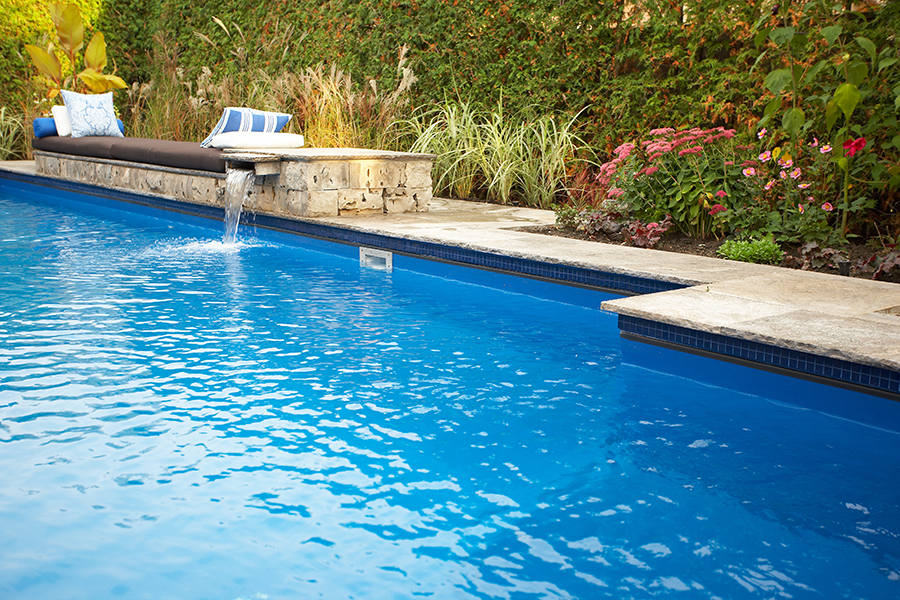 Vinyl inground pool with a stone spillover water feature and landscaped garden bed